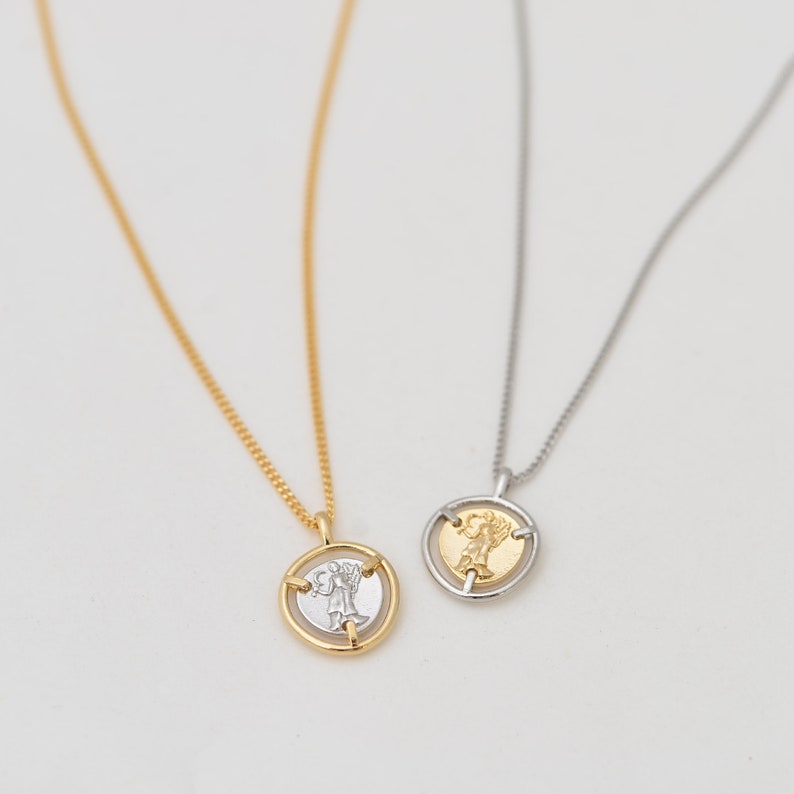 May include: Two delicate necklaces with a spinning coin pendant. One necklace has a gold chain and a gold coin with a silver angel design. The other necklace has a silver chain and a silver coin with a gold angel design.