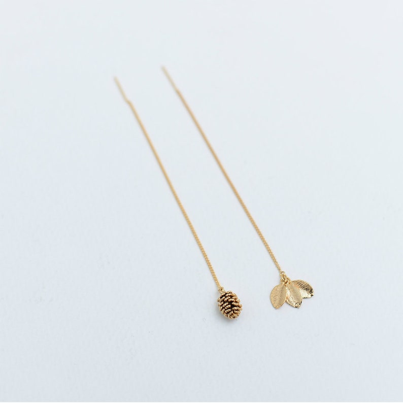 May include: A pair of gold dangle earrings with a pine cone charm on one earring and a leaf charm on the other.