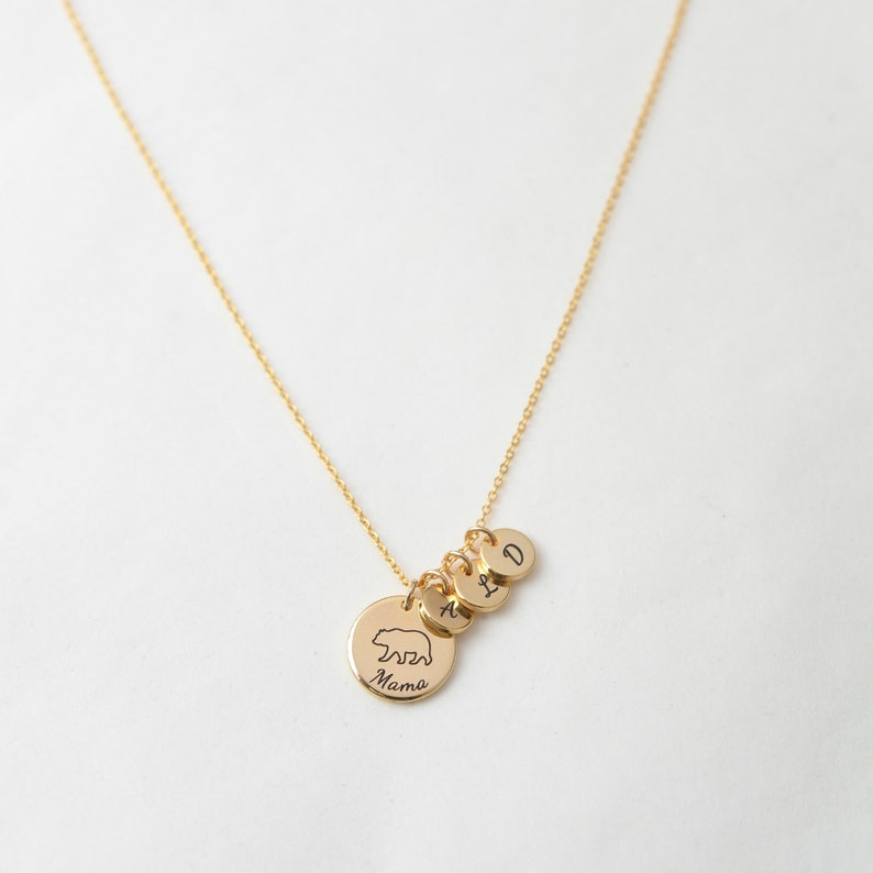 May include: Gold necklace with a bear charm and three initial charms. The bear charm says "Mama" on the back. The initials are A, I, and D.