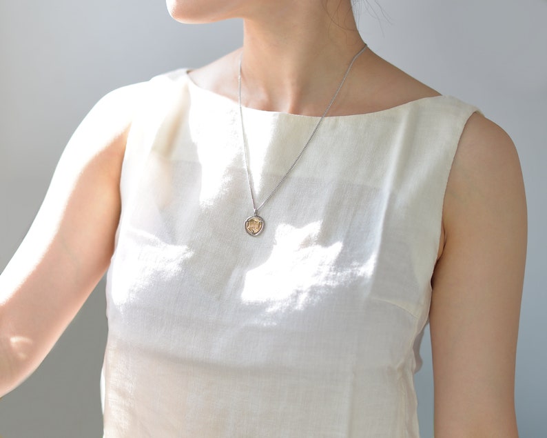 May include: A woman wearing a white sleeveless top with a silver chain necklace and a small gold pendant.