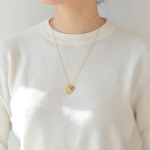 May include: A gold chain necklace with a round pendant that says "Stay Wild" and a smaller charm. The necklace is worn by a person wearing a white sweater.