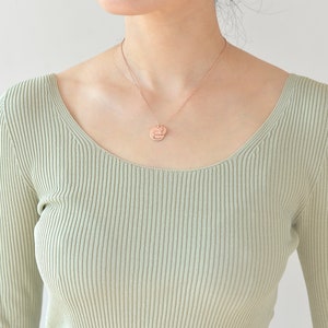 May include: A person wearing a light green ribbed sweater with a rose gold necklace and a round pendant.