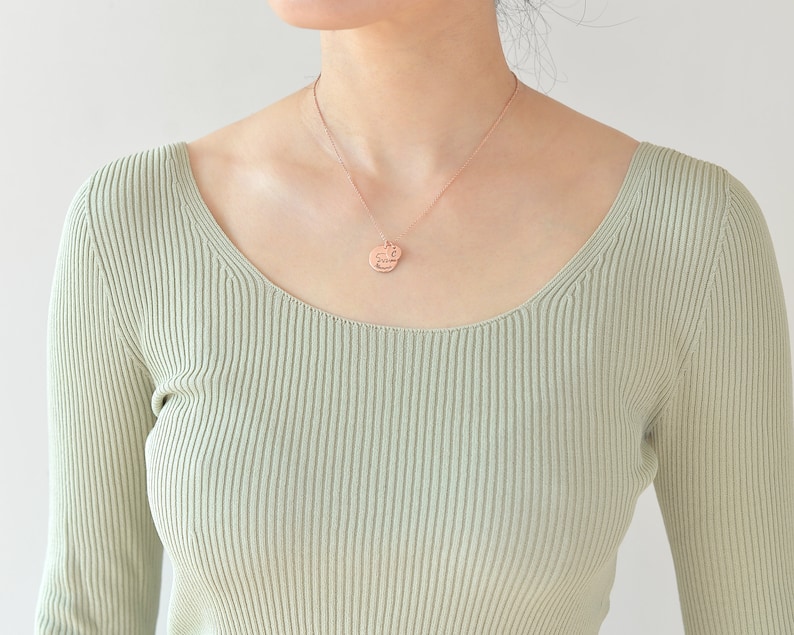 May include: A person wearing a light green ribbed sweater with a rose gold necklace and a round pendant.