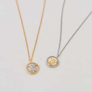 May include: Two gold necklaces with a round pendant featuring a detailed design. One necklace has a gold pendant and the other has a silver pendant.