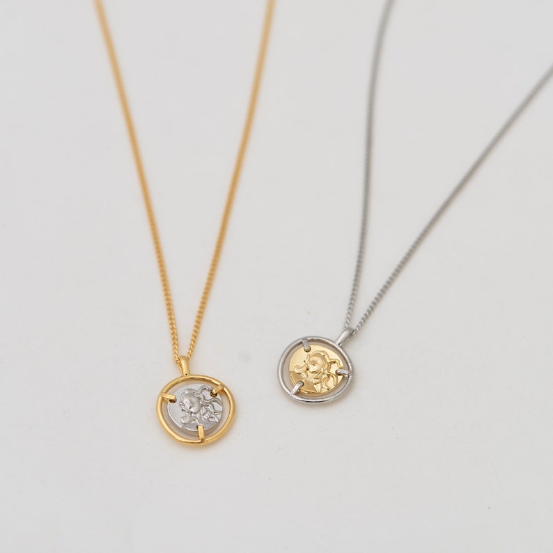 May include: Two gold necklaces with a round pendant featuring a detailed design. One necklace has a gold pendant and the other has a silver pendant.