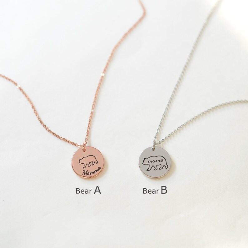 May include: Two silver necklaces with bear pendants. The pendant on the left is rose gold and says "Momma" with a bear outline. The pendant on the right is silver and says "mama" with a bear outline.