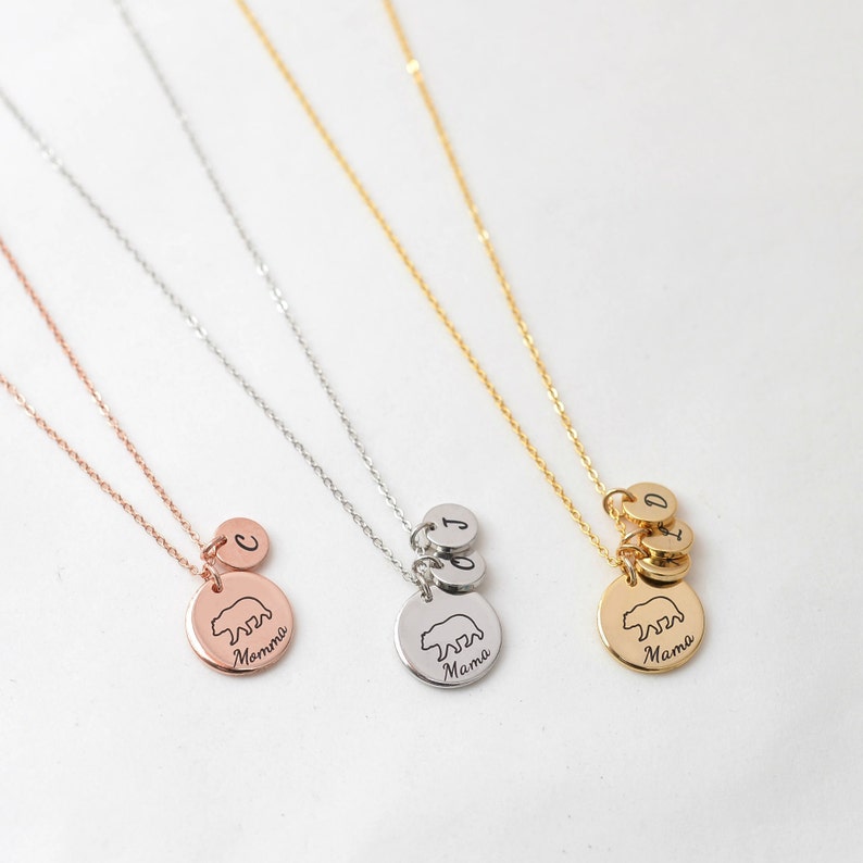 May include: Three gold, silver, and rose gold necklaces with bear pendants. Each pendant has the word "Mama" engraved on it. The necklaces also have small charms with letters on them.