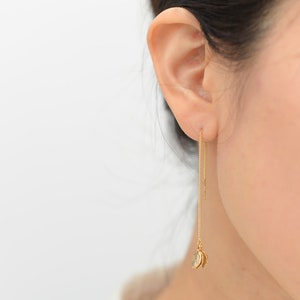 May include: Gold dangle earrings with two small leaf charms at the end of the chains.