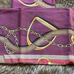 May include: Two burgundy pillowcases with a repeating pattern of gold-colored equestrian-themed designs, including chains, stirrups, and straps. The pillowcases have a striped border with pink and brown accents.