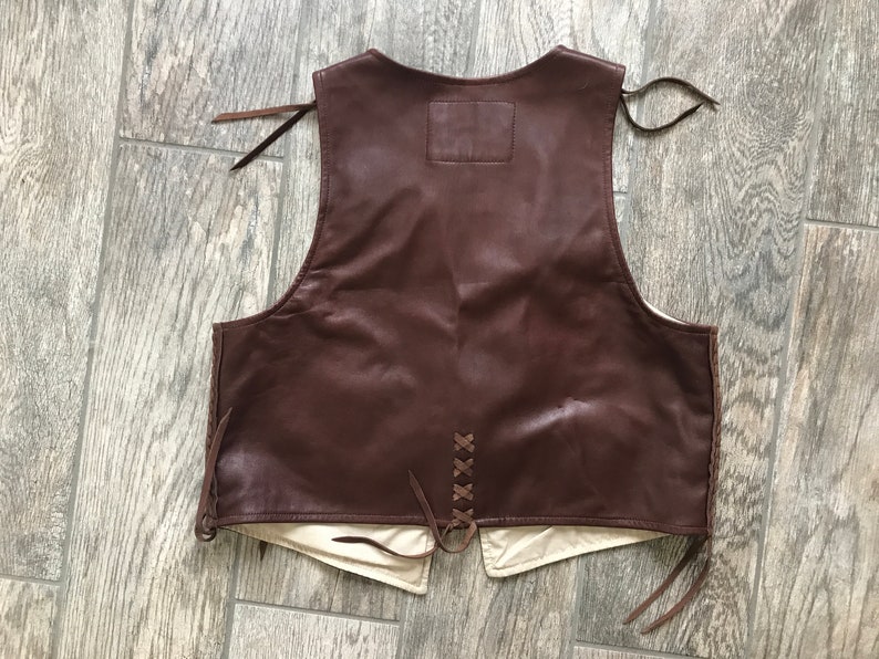 May include: A brown leather vest with a lace-up back and fringe detailing. The vest has a plain back with no pockets or embellishments.