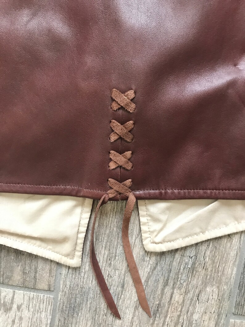 May include: A brown leather skirt with a lace-up back detail. The laces are brown and are tied in a knot at the bottom.