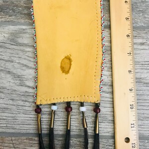 Puede incluir: Una peque&ntilde;a bolsa de cuero con cuentas y flecos de crin de caballo negro. La bolsa est&aacute; decorada con cuentas rojas, blancas y azules. Mide aproximadamente 15 cm de largo y 5 cm de ancho.