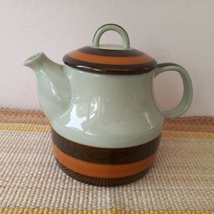 May include: A ceramic teapot with a brown, orange and green striped design. The teapot has a lid with a handle and a spout.
