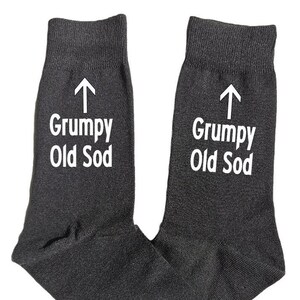 Könnte beinhalten: Ein Paar dunkelgraue Socken mit dem weißen Aufdruck "Grumpy Old Sod" und einem weißen Pfeil nach oben. Die Socken sind aus weichem Material und für den täglichen Gebrauch geeignet.