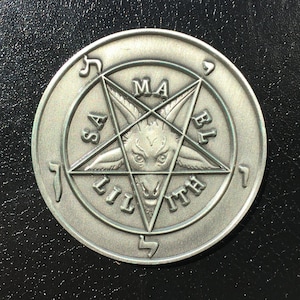 May include: A silver-colored metal coin with a pentagram design. The pentagram has the words "Samael" and "Lilith" inscribed on it, and a goat's head is in the center. The coin has a raised edge.