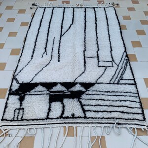 May include: A white and black Moroccan rug with a geometric pattern. The rug has a fringe border.