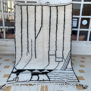 May include: A white and black Moroccan rug with a geometric design. The rug has a fringe border and is made of wool.