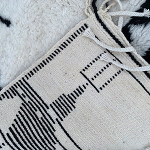 May include: A white and black geometric patterned rug with fringe. The rug has a simple design with black lines and squares on a white background.