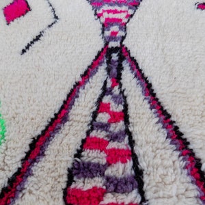 May include: Close-up of a white, fluffy rug with a geometric pattern in pink, purple, and black. The rug has a soft, textured surface.