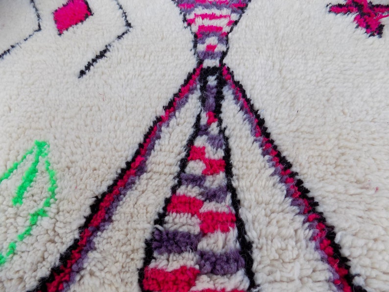 May include: Close-up of a white, fluffy rug with a geometric pattern in pink, purple, and black. The rug has a soft, textured surface.
