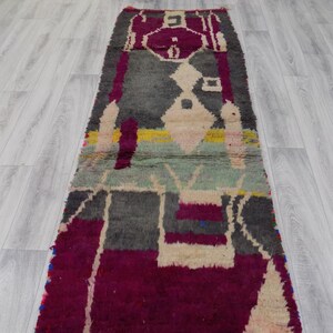 May include: A long, rectangular rug with a geometric pattern in shades of gray, beige, pink, and yellow. The rug has a fringed edge and is made of wool.