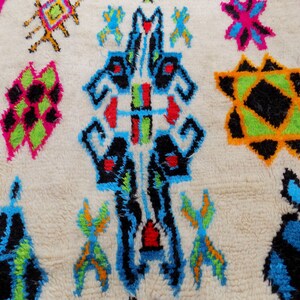 May include: A white rug with a colorful geometric pattern. The pattern features black, blue, green, red, orange, and yellow colors. The rug has a fluffy texture.