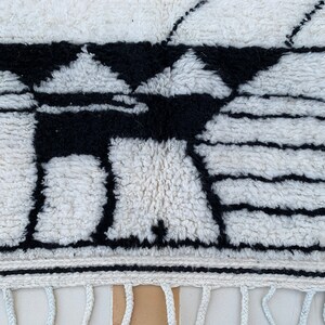 May include: Black and white geometric pattern woven into a white rug with a fringe border.