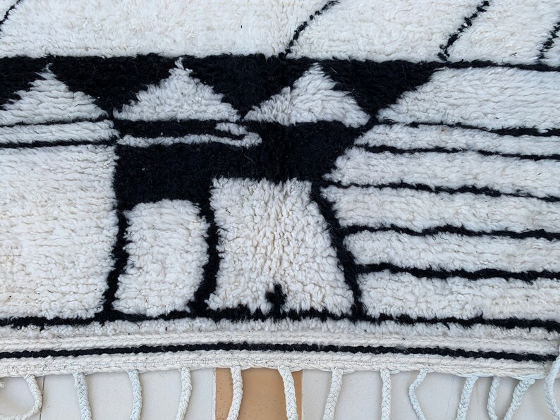 May include: Black and white geometric pattern woven into a white rug with a fringe border.