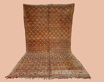 May include: A vintage Moroccan rug with a geometric pattern in shades of orange, brown, and white. The rug has a fringe border.