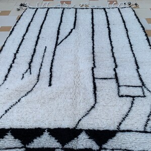 May include: A white and black Moroccan rug with a geometric pattern. The rug has a fringe border and is made of wool.