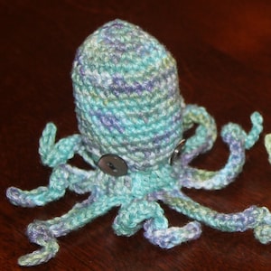 May include: A crocheted octopus toy with blue, green, and purple yarn. The octopus has eight tentacles and two black buttons for eyes.