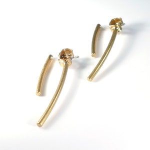 May include: A pair of gold-toned earrings with a curved bar design. The earrings are made of a smooth, polished metal.