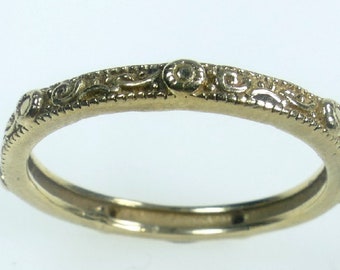 May include: A gold band ring with a delicate, intricate design. The ring is smooth and polished, with a subtle shine.