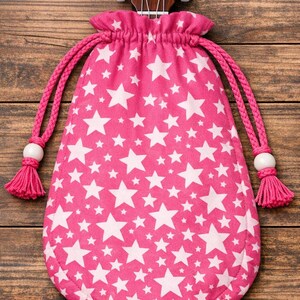 Könnte beinhalten: Ein pinkfarbener Kordelzugbeutel mit weißem Sternmuster, der für eine Ukulele bestimmt ist. Der Beutel hat geflochtene pinkfarbene Kordeln mit weißen Perlen und pinkfarbenen Quasten. Der Kopf der Ukulele ist über dem Beutel sichtbar.