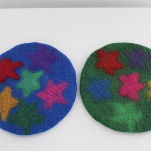 May include: Two round felt coasters with a green and blue background. Each coaster has a different arrangement of colorful stars.