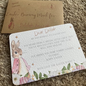 May include: A white card with a watercolor illustration of a bunny rabbit wearing a pink jacket. The card has the text "Dear Delilah" and a message about Easter. The card is decorated with flowers and eggs.