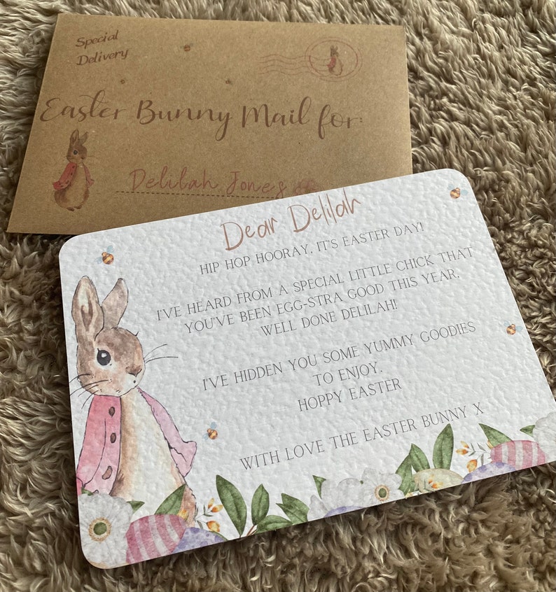 May include: A white card with a watercolor illustration of a bunny rabbit wearing a pink jacket. The card has the text "Dear Delilah" and a message about Easter. The card is decorated with flowers and eggs.