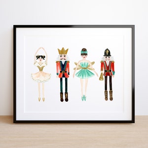 May include: A framed print with watercolour illustrations of four Nutcracker characters. The characters include a ballerina in a gold tutu, a nutcracker soldier, a fairy in a teal dress, and a soldier with a trumpet. The artwork is set against a white background.