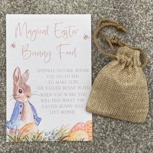 May include: A white card with pink text that reads "Magical Easter Bunny Food". The card features an illustration of a bunny rabbit holding a blue jacket and surrounded by colourful eggs. The card also includes instructions to sprinkle the food outside before bed to make sure the Easter bunny is fed. A small hessian bag is included.