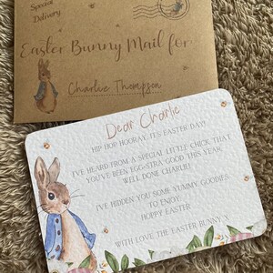 May include: A white card with a watercolor illustration of Peter Rabbit. The card has a pink and white floral border and the text "Dear Charlie, HIP HOP HOORAY. IT'S EASTER DAY! I'VE HEARD FROM A SPECIAL LITTLE CHICK THAT YOU'VE BEEN EGG-STRA GOOD THIS YEAR. WELL DONE CHARLIE! I'VE HIDDEN YOU SOME YUMMY GOODIES TO ENJOY. HOPPY EASTER WITH LOVE THE EASTER BUNNY X".