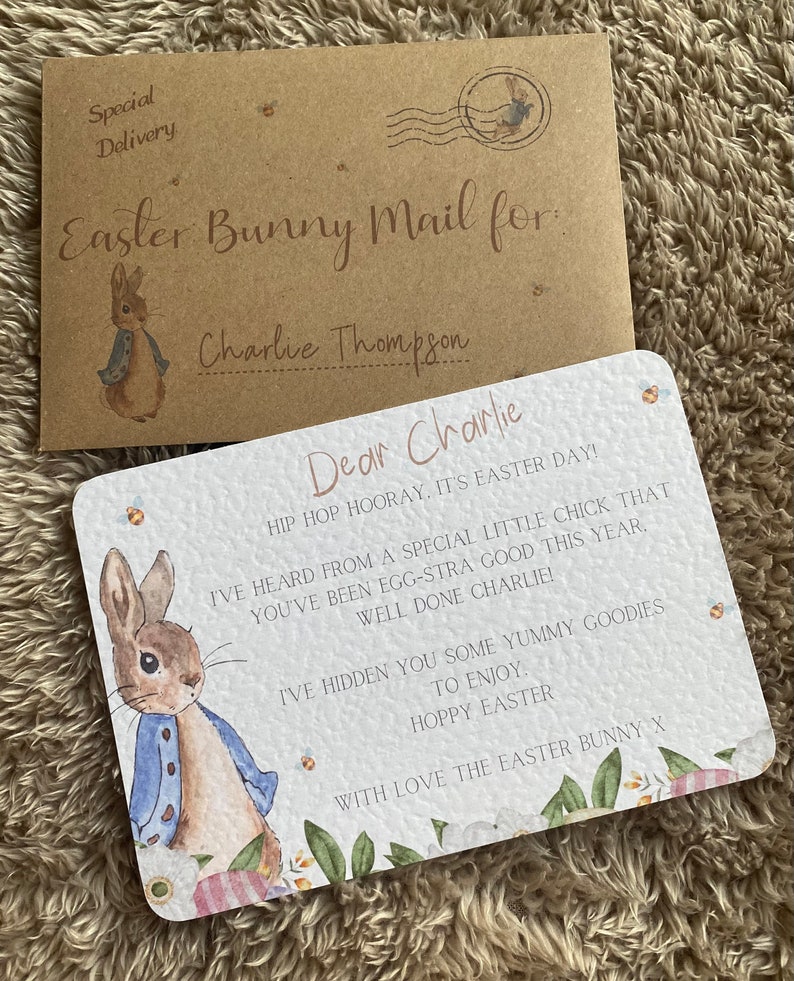 May include: A white card with a watercolor illustration of Peter Rabbit. The card has a pink and white floral border and the text "Dear Charlie, HIP HOP HOORAY. IT'S EASTER DAY! I'VE HEARD FROM A SPECIAL LITTLE CHICK THAT YOU'VE BEEN EGG-STRA GOOD THIS YEAR. WELL DONE CHARLIE! I'VE HIDDEN YOU SOME YUMMY GOODIES TO ENJOY. HOPPY EASTER WITH LOVE THE EASTER BUNNY X".