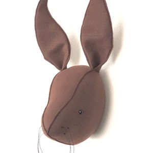 May include: A brown felt rabbit head wall decor with black felt eyes and whiskers.