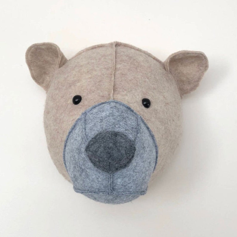 May include: A beige felt bear head wall decor with a gray felt nose and black button eyes.