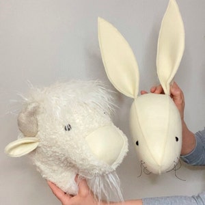 May include: Two white felt animal head wall decorations. The first is a fluffy white bison with a long beard. The second is a white rabbit with long ears.