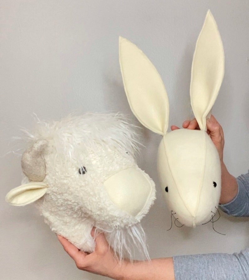 May include: Two white felt animal head wall decorations. The first is a fluffy white bison with a long beard. The second is a white rabbit with long ears.