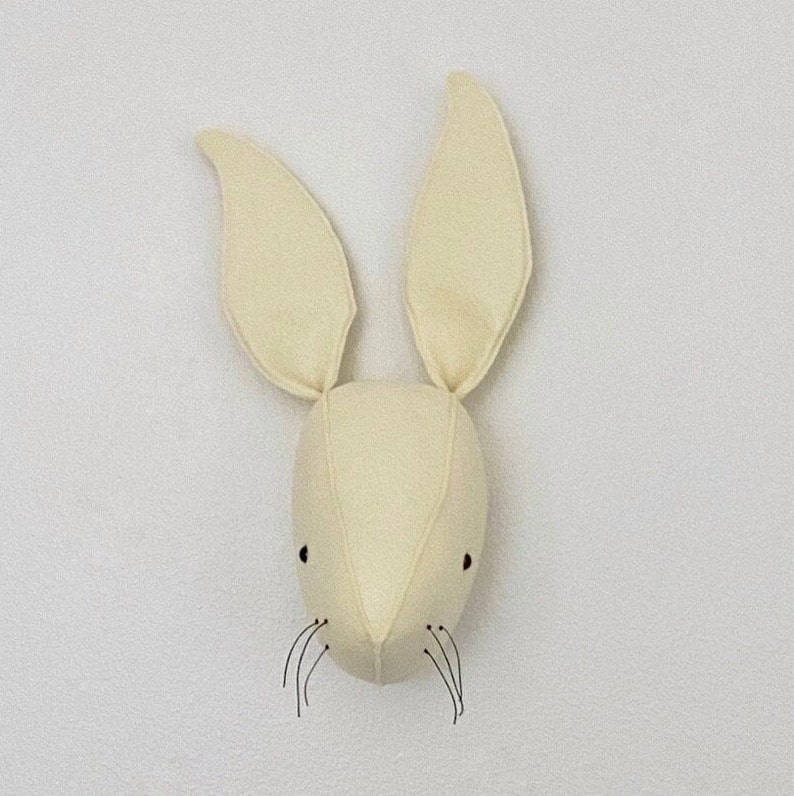 May include: A cream-colored felt bunny head with black eyes and whiskers. The bunny head is a wall decoration.
