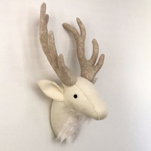 May include: A white felt deer head wall mount with brown felt antlers. The deer head has a fluffy white beard and black eyes.