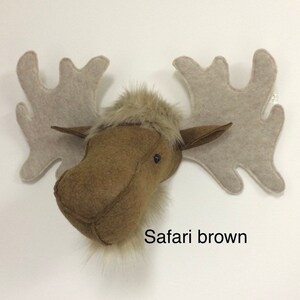 May include: A brown felt moose head with a furry face and large, light brown felt antlers. The text "Safari brown" is printed below the moose head.