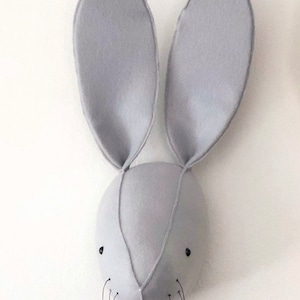 May include: A gray felt bunny head wall decor with long ears and black embroidered eyes. The bunny has a small nose and whiskers.