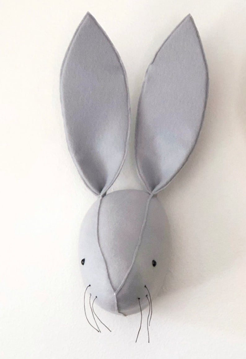 May include: A gray felt bunny head wall decor with long ears and black embroidered eyes. The bunny has a small nose and whiskers.